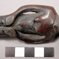 Wooden figurine, carved in human effigy: female(?), hands resting on flexed knee
