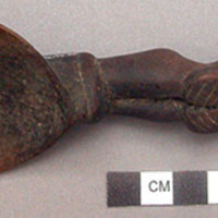 Wooden spoon, handle carved in human effigy: hands resting on flexed knees, coil