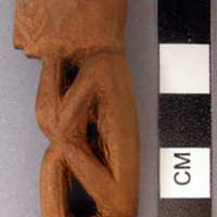 Carved wooden bottle stopper figure of man with hands on face, elbows on knees.